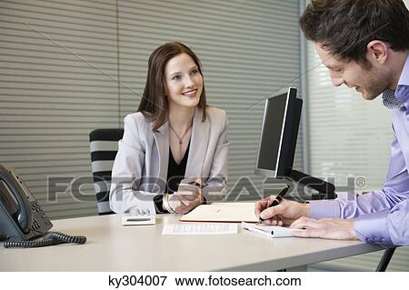 Man signing documents with a female real estate agent sitting in front of him View Large Photo Image Stock Photo - Man signing documents with a female real estate agent sitting in front of him. Fotosearch