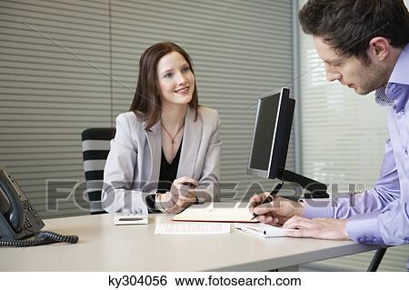 Man signing documents with a female real estate agent sitting in front of him View Large Photo Image Stock Photograph - Man signing documents with a female real estate agent sitting in front of him. Fotosearch