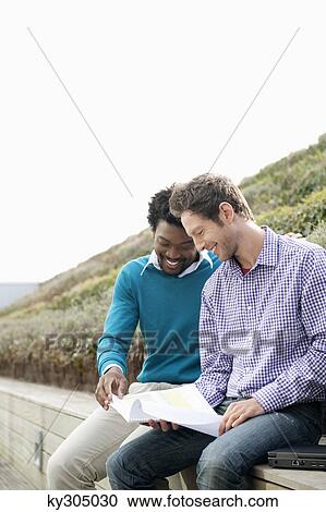 Stock Image - Friends discussing documents on a boardwalk. Fotosearch