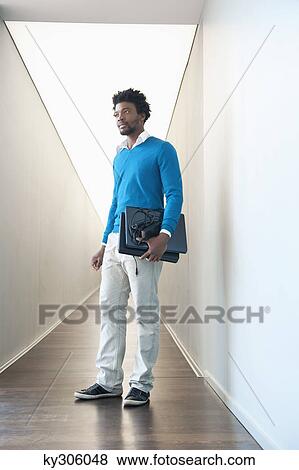 Stock Photo - Businessman carrying two laptops in the corridor of an office. Fotosearch