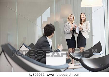 Stock Image - Businessman sitting in a waiting room looking at his colleagues smiling in the background. Fotosearch
