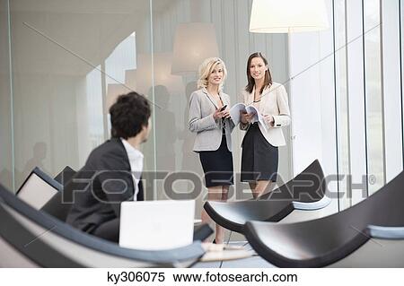 Stock Photography - Businessman sitting in a waiting room looking at his colleagues standing in the background. Fotosearch