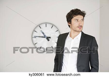 Stock Image - Businessman standing in front of a clock. Fotosearch