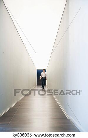 Businessman walking in the corridor of an office View Large Photo Image Stock Photography - Businessman walking in the corridor of an office. Fotosearch
