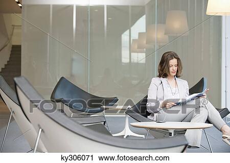 Businesswoman sitting on a chair and reading a magazine View Large Photo Image Stock Image - Businesswoman sitting on a chair and reading a magazine. Fotosearch