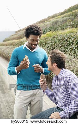 Two friends eating sandwiches on a boardwalk View Large Photo Image Stock Photography - Two friends eating sandwiches on a boardwalk. Fotosearch