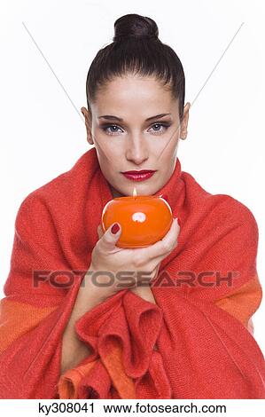 Stock Image - Young woman wrapped in blanket, holding candle. Fotosearch