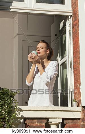 Stock Image - Young woman enjoying sun at window. Fotosearch