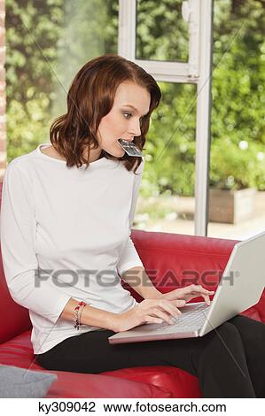 Young woman holding credit card in mouth, using laptop View Large Photo Image Stock Image - Young woman holding credit card in mouth, using laptop. Fotosearch