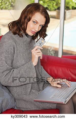 Stock Image - Young woman holding credit card, using laptop. Fotosearch