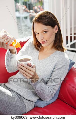 Stock Image - Young woman pouring honey into her tea cup. Fotosearch