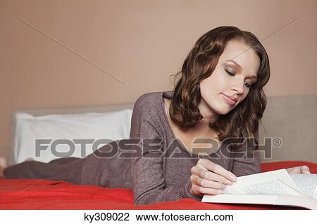 Stock Image - Young woman reading a book in bed. Fotosearch