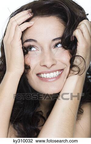Stock Image - Young woman smiling with hands in hair. Fotosearch