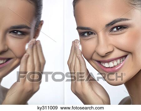Stock Photo - Young woman applying moisturizer and her reflection in mirror. Fotosearch
