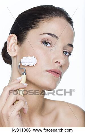 Stock Photograph - Young woman using facial massage roller. Fotosearch