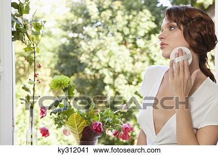Stock Image - Young woman applying face powder. Fotosearch