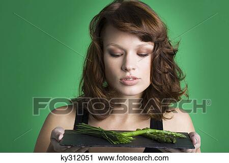 Stock Image - Young woman holding tray of asparagus and chives. Fotosearch