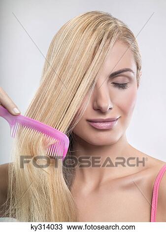 Stock Image - Young woman combing hair. Fotosearch