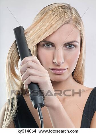 Picture - Young woman using hair straighteners. Fotosearch