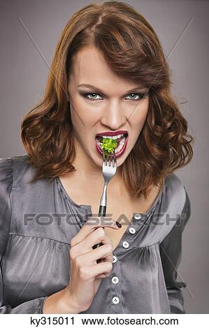 Stock Image - Young woman eating broccoli. Fotosearch