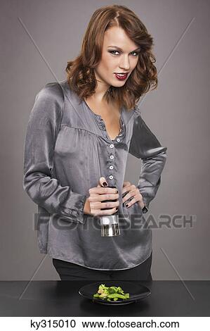 Stock Image - Young woman seasoning vegetables. Fotosearch