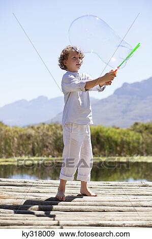 Stock Photo - Boy playing with a bubble wand at a pier. Fotosearch