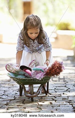 Stock Photo - Cute girl pushing a wheelbarrow filled with toys. Fotosearch