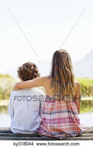 Picture - Rear view of siblings sitting together at a pier. Fotosearch