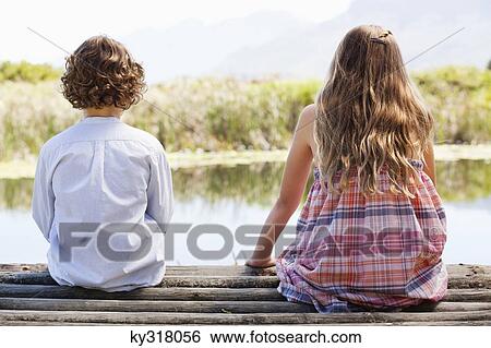 Rear view of siblings sitting together at a pier View Large Photo Image Stock Photograph - Rear view of siblings sitting together at a pier. Fotosearch