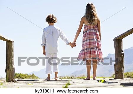 Stock Image - Rear view of siblings standing together at a pier. Fotosearch