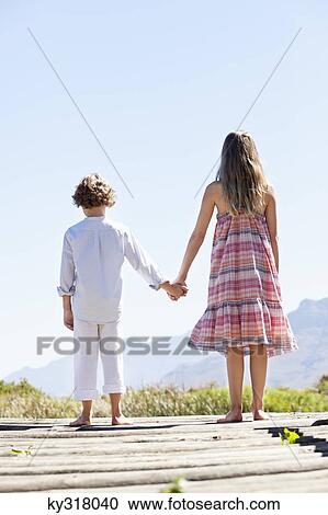 Rear view of siblings standing together at a pier View Large Photo Image Stock Image - Rear view of siblings standing together at a pier. Fotosearch