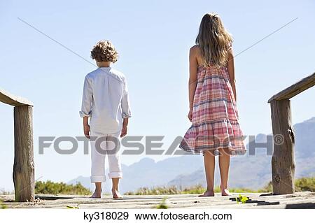 Rear view of siblings standing together at a pier View Large Photo Image Stock Photo - Rear view of siblings standing together at a pier. Fotosearch