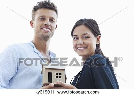 Stock Image - Portrait of a young couple holding a small model house. Fotosearch