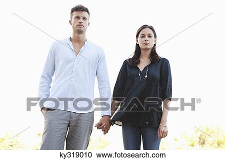 Stock Image - Portrait of a young couple holding hands standing together. Fotosearch