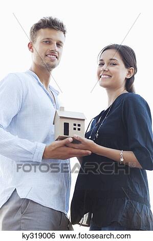 Stock Photograph - Portrait of a young couple holding small model house. Fotosearch