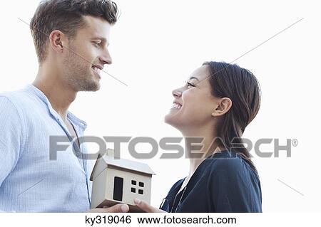 Profile of a young couple holding small model house and looking at each other View Large Photo Image Stock Photograph - Profile of a young couple holding small model house and looking at each other. Fotosearch