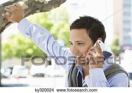 Close-up of a mid adult man holding a branch of tree talking on a mobile phone View Large Photo Image Picture - Close-up of a mid adult man holding a branch of tree talking on a mobile phone. Fotosearch