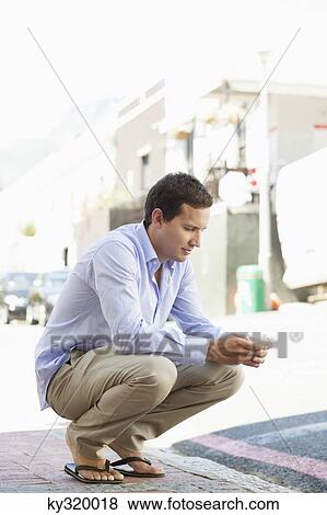 Man crouching and text messaging on a mobile phone View Large Photo Image Stock Photo - Man crouching and text messaging on a mobile phone. Fotosearch