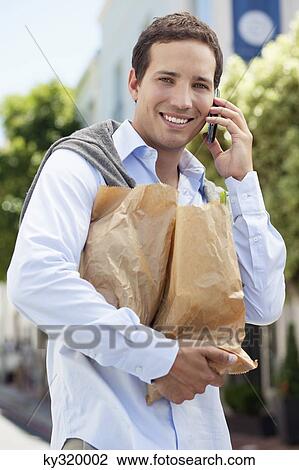 Mid adult man talking on a mobile phone with paper bags full of vegetables View Large Photo Image Stock Image - Mid adult man talking on a mobile phone with paper bags full of vegetables. Fotosearch
