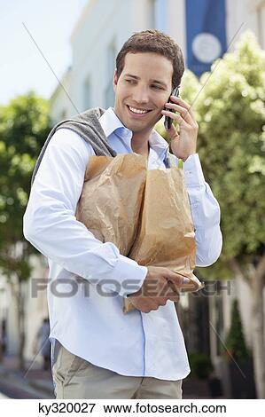 Mid adult man talking on a mobile phone with paper bags full of vegetables View Large Photo Image Stock Photo - Mid adult man talking on a mobile phone with paper bags full of vegetables. Fotosearch