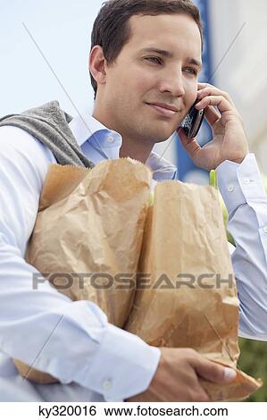 Mid adult man talking on a mobile phone with paper bags full of vegetables View Large Photo Image Stock Photograph - Mid adult man talking on a mobile phone with paper bags full of vegetables. Fotosearch