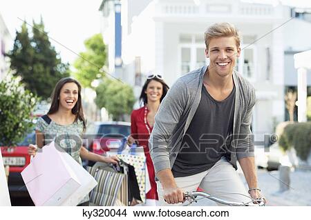Young man cycling with two women standing in the background View Large Photo Image Picture - Young man cycling with two women standing in the background. Fotosearch