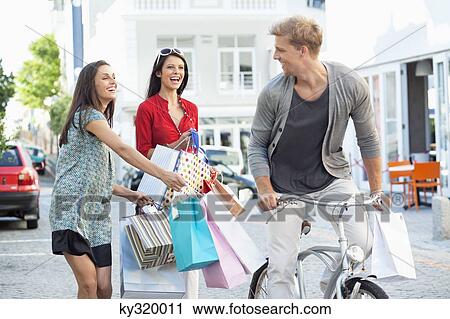 Young man cycling with two women running after him with shopping bags View Large Photo Image Stock Image - Young man cycling with two women running after him with shopping bags. Fotosearch