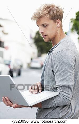 Young man using a laptop on a street View Large Photo Image Stock Photograph - Young man using a laptop on a street. Fotosearch