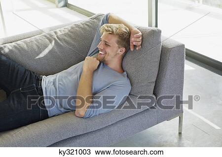 High angle view of a young man lying on a couch at home and smiling View Large Photo Image Stock Image - High angle view of a young man lying on a couch at home and smiling. Fotosearch