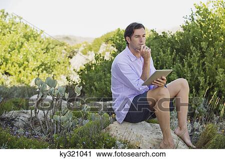 Man sitting on a rock using a digital tablet and thinking View Large Photo Image Stock Image - Man sitting on a rock using a digital tablet and thinking. Fotosearch