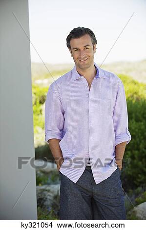 Man standing with his hands in his pockets and smiling View Large Photo Image Picture - Man standing with his hands in his pockets and smiling. Fotosearch