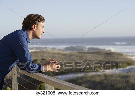 Stock Photo - Mid adult man leaning on a railing of a balcony. Fotosearch