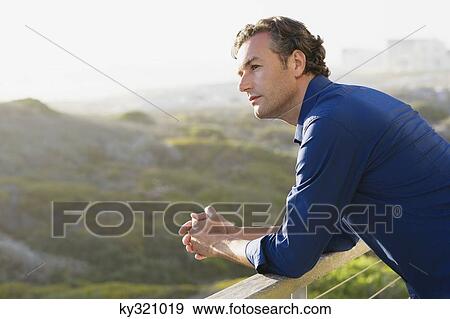 Mid adult man leaning on a railing of a balcony View Large Photo Image Stock Photo - Mid adult man leaning on a railing of a balcony. Fotosearch
