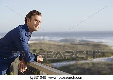 Stock Photography - Mid adult man leaning on a railing of a balcony. Fotosearch